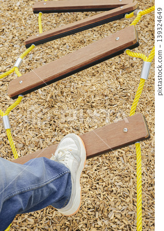 Person foot stepping on a wooden balance plank in a playground. Childishness und playful movement. Person foot stepping on a wooden balance plank in a playground. Childishness und playful movement. 139324649