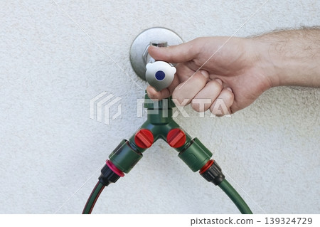Hand turning an outdoor water faucet with a dual hose connector, highlighting efficient water control and sustainable use. Hand turning an outdoor water faucet with a dual hose connector, highlighting efficient water control and sustainable use. 139324729