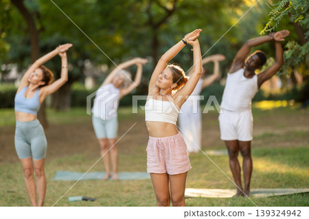 Girl doing Nitambasana at group yoga class in park Girl doing Nitambasana at group yoga class in park 139324942