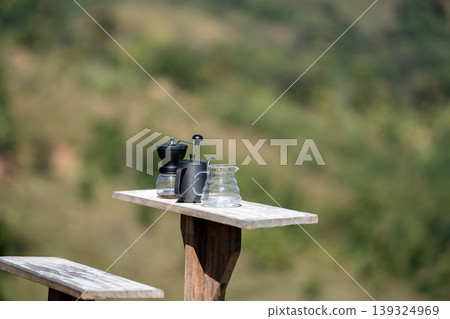 The coffee grinder, kettle, and coffee pot arranged on the table at the beautiful flower field view above the forest and mountains background 139324969