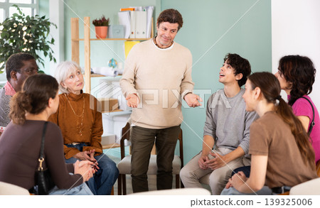 Positive man standing communicating with group of adult people at seminar in advanced training Positive man standing communicating with group of adult people at seminar in advanced training 139325006