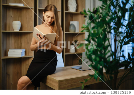 Woman reading a book in a modern office space during daytime hours Woman reading a book in a modern office space during daytime hours 139325139
