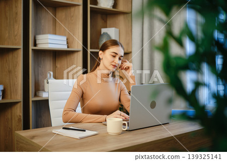 Woman working on laptop in modern home office during daytime 139325141