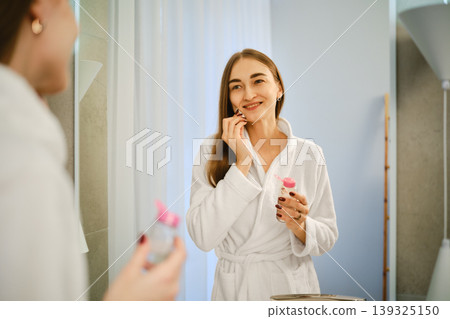 Woman applying skincare in bathroom while looking in mirror during morning routine Woman applying skincare in bathroom while looking in mirror during morning routine 139325150