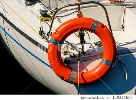 Close-up of orange lifebuoy attached to boat deck, essential marine safety equipment with ropes and fittings, nautical transport concept Close-up of orange lifebuoy attached to boat deck, essential marine safety equipment with ropes and fittings, nautical transport concept 139325605