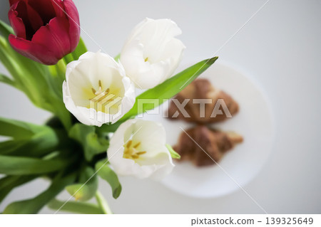 White and red tulips in a vase and croissants on a plate in the background White and red tulips in a vase and croissants on a plate in the background 139325649