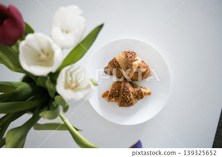 Tho croissants on a plate with white and red tulips in the foreground Tho croissants on a plate with white and red tulips in the foreground 139325652