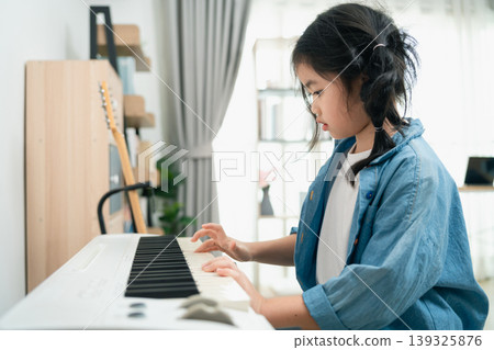 Young girl plays piano at home in cozy living room while wearing a denim jacket and focusing on her musical practice and creativity development Young girl plays piano at home in cozy living room while wearing a denim jacket and focusing on her musical practice and creativity development 139325876