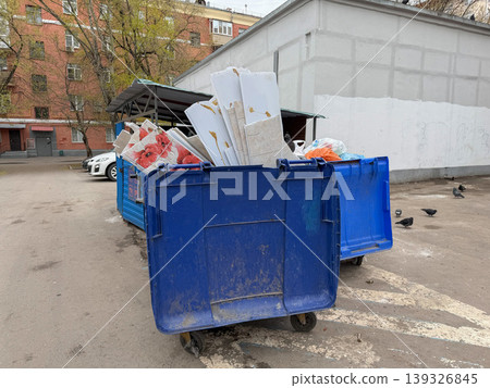 Overflowing garbage containers with mixed waste near residential building in urban yard environment. Waste management, urban sanitation, environmental problem, recycling, city infrastructure Overflowing garbage containers with mixed waste near residential building in urban yard environment. Waste management, urban sanitation, environmental problem, recycling, city infrastructure 139326845