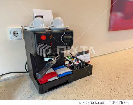 Coffee machine with cups and condiments on countertop in hotel room interior with power outlet, wall background. Hospitality service, travel accommodation, business stay, guest comfort, hotel amenity Coffee machine with cups and condiments on countertop in hotel room interior with power outlet, wall background. Hospitality service, travel accommodation, business stay, guest comfort, hotel amenity 139326863