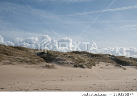 Sand dunes with grass, textured beach surface under blue sky with clouds in Belgium coastal area. Travel destination, tourism marketing, coastal landscape, nature background, outdoor environment Sand dunes with grass, textured beach surface under blue sky with clouds in Belgium coastal area. Travel destination, tourism marketing, coastal landscape, nature background, outdoor environment 139326874