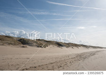 Wide sandy beach with dunes, tracks under blue sky with clouds along North Sea coast in Belgium. Travel destination, tourism marketing, coastal landscape, outdoor recreation, nature background Wide sandy beach with dunes, tracks under blue sky with clouds along North Sea coast in Belgium. Travel destination, tourism marketing, coastal landscape, outdoor recreation, nature background 139326875