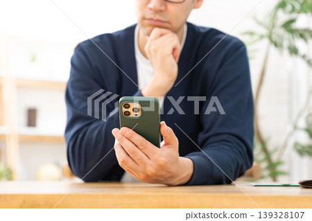 A man looking at his smartphone and pondering A man looking at his smartphone and pondering 139328107