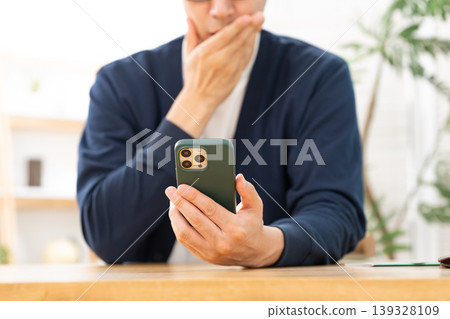 一個男人看著他的智慧型手機,若有所思。 一個男人看著他的智慧型手機,若有所思。 139328109
