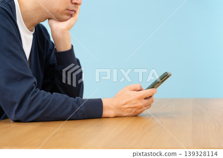 一名男子正低頭看著他的智慧型手機,似乎心事重重;他的雙手併攏在身側。 一名男子正低頭看著他的智慧型手機,似乎心事重重;他的雙手併攏在身側。 139328114