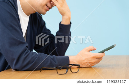 A man looking at his smartphone, seemingly troubled; his hands are close up, sideways. A man looking at his smartphone, seemingly troubled; his hands are close up, sideways. 139328117