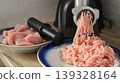 A black electric meat grinder on a kitchen countertop against a gray wall with two plates of pink poultry fillets and ready-made minced meat, minced on a household appliance 139328164