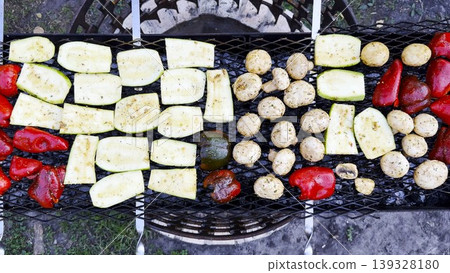 Top view on vegetables roasting on home grill over open heat. Smoke rises gently as meal cook developing lightly charred surface. The focus on grilling process texture and appetizing appearance Top view on vegetables roasting on home grill over open heat. Smoke rises gently as meal cook developing lightly charred surface. The focus on grilling process texture and appetizing appearance 139328180