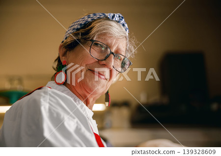 Portrait of smiling senior woman with blue headband in bright kitchen setting Portrait of smiling senior woman with blue headband in bright kitchen setting 139328609