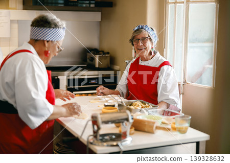 Smiling senior woman looking at camera while baking with friends in kitchen Smiling senior woman looking at camera while baking with friends in kitchen 139328632