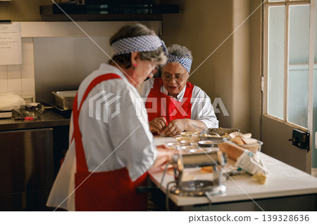 Senior women in aprons preparing handmade pastries together in a professional kitchen Senior women in aprons preparing handmade pastries together in a professional kitchen 139328636
