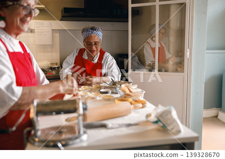 Senior woman filling small pastry tins with savory mixture in a kitchen environment 139328670