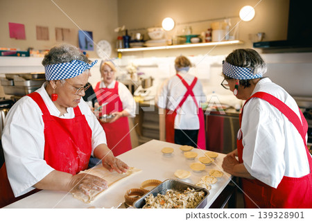 Senior African American and Caucasian women baking together in a professional kitchen setting Senior African American and Caucasian women baking together in a professional kitchen setting 139328901