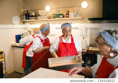 Senior Black and Caucasian women in red aprons working together in a community kitchen setting 139328912