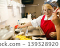 Senior Caucasian Woman Chef Preparing Healthy Food in Professional Kitchen Setting 139328920