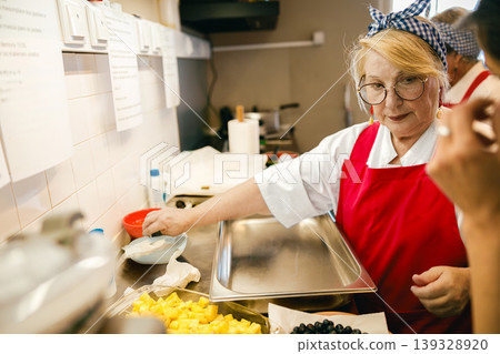 Senior Caucasian Woman Chef Preparing Healthy Food in Professional Kitchen Setting 139328920