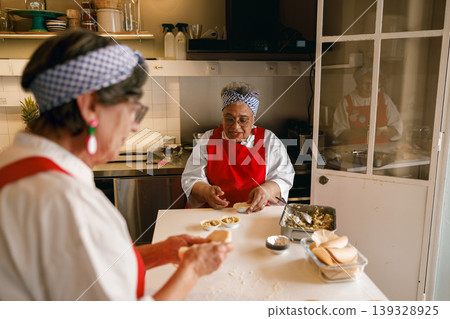 Senior Caucasian and Black Women Bakers Preparing Pastries in Commercial Kitchen Senior Caucasian and Black Women Bakers Preparing Pastries in Commercial Kitchen 139328925