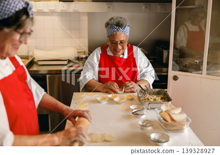 Senior Black and Caucasian women chefs preparing pastries in a commercial kitchen bakery Senior Black and Caucasian women chefs preparing pastries in a commercial kitchen bakery 139328927
