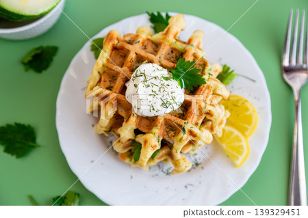 crispy zucchini waffles with sour cream and lemon slices on plate 139329451
