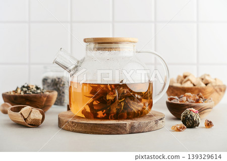 Blooming tea in a glass teapot with dry tea leaves, brown sugar in bowls, and ingredients on a light background. 139329614
