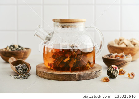 Blooming tea in a glass teapot with dry tea leaves, brown sugar in bowls, and ingredients on a light background. 139329616