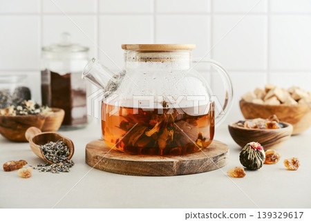 Blooming tea in a glass teapot with dry tea leaves, brown sugar in bowls, and ingredients on a light background. 139329617