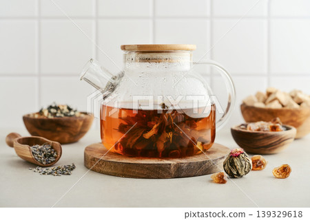 Blooming tea in a glass teapot with dry tea leaves, brown sugar in bowls, and ingredients on a light background. 139329618