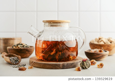 Blooming tea in a glass teapot with dry tea leaves, brown sugar in bowls, and ingredients on a light background. 139329619