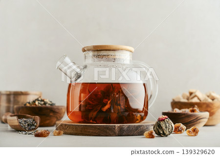 Blooming tea in a glass teapot with dry tea leaves, brown sugar in bowls, and ingredients on a light background. 139329620