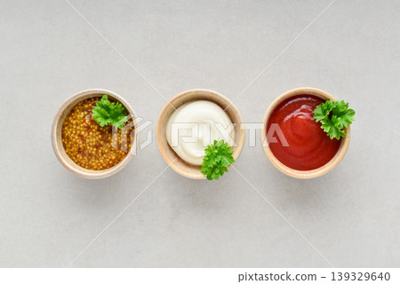 Top view of three small bowls with mayonnaise, ketchup, and mustard arranged in a row on a light background Top view of three small bowls with mayonnaise, ketchup, and mustard arranged in a row on a light background 139329640