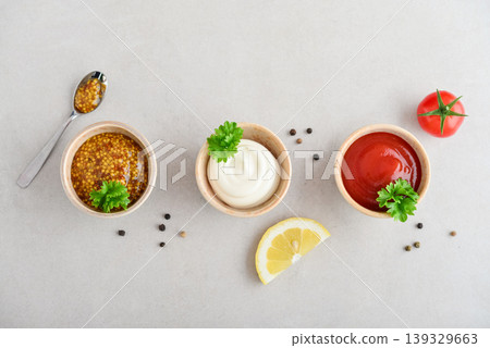 Top view of three small bowls with mayonnaise, ketchup, and mustard arranged in a row on a light background Top view of three small bowls with mayonnaise, ketchup, and mustard arranged in a row on a light background 139329663