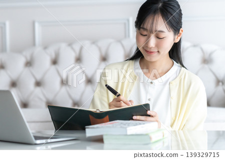 一位面帶微笑的女士在家裡的客廳裡用日程表寫著她的計劃表。內容包括生活方式、事業、學習和自我提升。 一位面帶微笑的女士在家裡的客廳裡用日程表寫著她的計劃表。內容包括生活方式、事業、學習和自我提升。 139329715