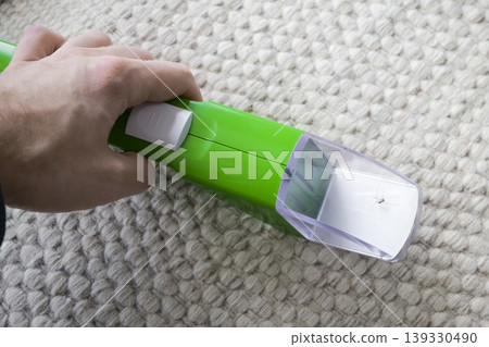 Hand holding a green insect trap with a spider inside, against a textured carpet background. Hand holding a green insect trap with a spider inside, against a textured carpet background. 139330490