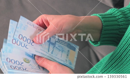 Female hands counting and organizing stacks of blue currency notes on a gray surface, showcasing the detailed design and denomination of the bills Female hands counting and organizing stacks of blue currency notes on a gray surface, showcasing the detailed design and denomination of the bills 139330561