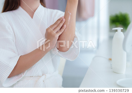 Asian women apply body lotion cream moisturizer on arm skin after shower in white bathroom for smooth hydration skincare morning routine wellness selfcare at 139330729