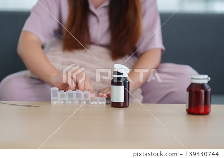 Asian women organizing medicine pills daily medication supplement vitamin sitting home table health wellness routine morning healthcare management pharmacy 139330744