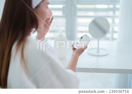 Asian women applying skincare product morning routine using mirror compact beauty cosmetic moisturizer face care treatment white bathrobe home bathroom hygiene Asian women applying skincare product morning routine using mirror compact beauty cosmetic moisturizer face care treatment white bathrobe home bathroom hygiene 139330758
