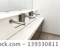 Minimalist public restroom with sleek stainless steel faucets and a white counter, emphasizing cleanliness, hygiene, and modern interior design. 139330811