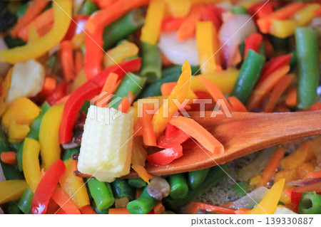 Cooking fresh colorful vegetable mix with baby corn and green beans using wooden spatula in a pan 139330887