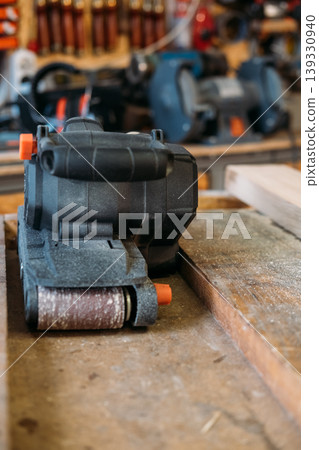 Carpentry equipment. Belt sander. Portable electric power joinery tool for professional work on wooden sawdust board in garage interior. 139330940